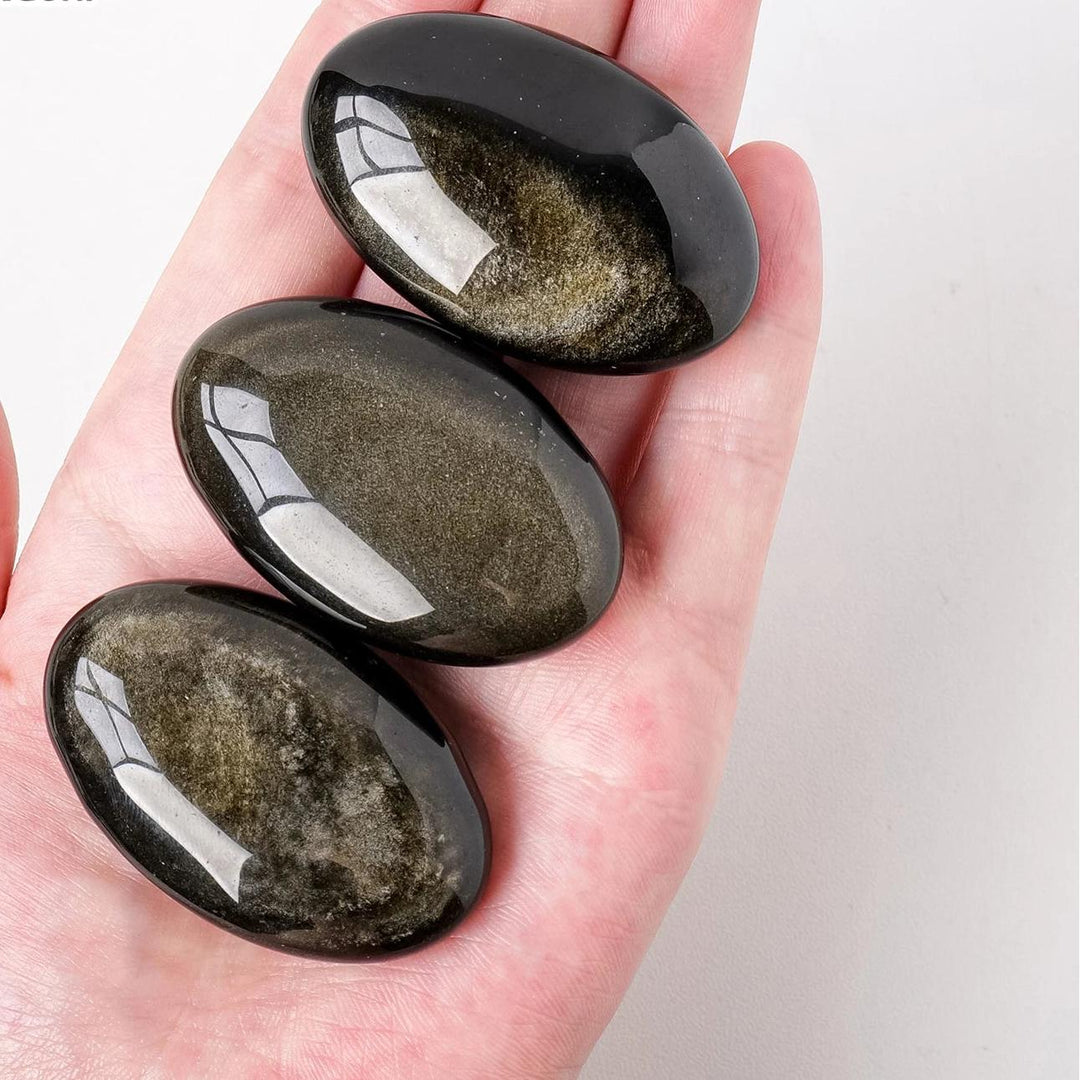 Three smooth, polished Gold Sheen Obsidian palm stones with a deep black base and glowing golden shimmer for grounding.