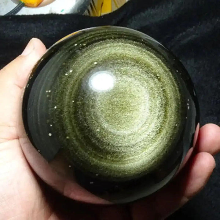Hand-polished Gold Sheen Obsidian sphere featuring a mesmerizing golden glow and protective volcanic glass energy.
