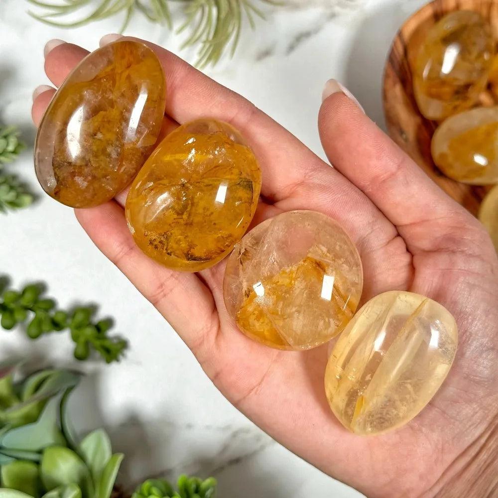 Hand holding four smooth, polished Golden Healer Quartz palm stones with warm, amber-toned iron-rich inclusions.