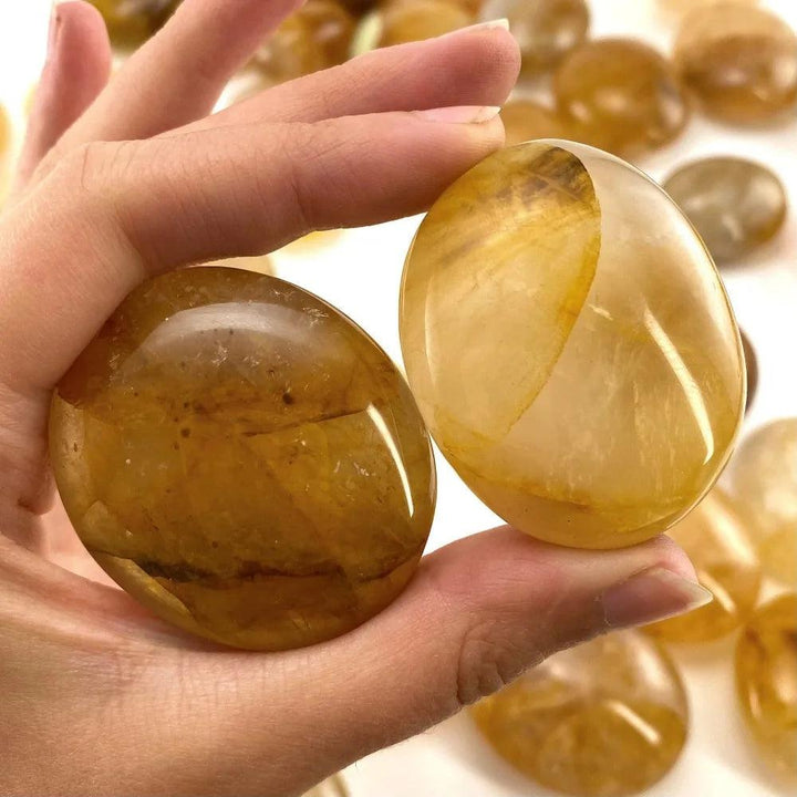 Polished Golden Healer Quartz palm stone with amber glow and iron-rich inclusions for healing and manifestation.
