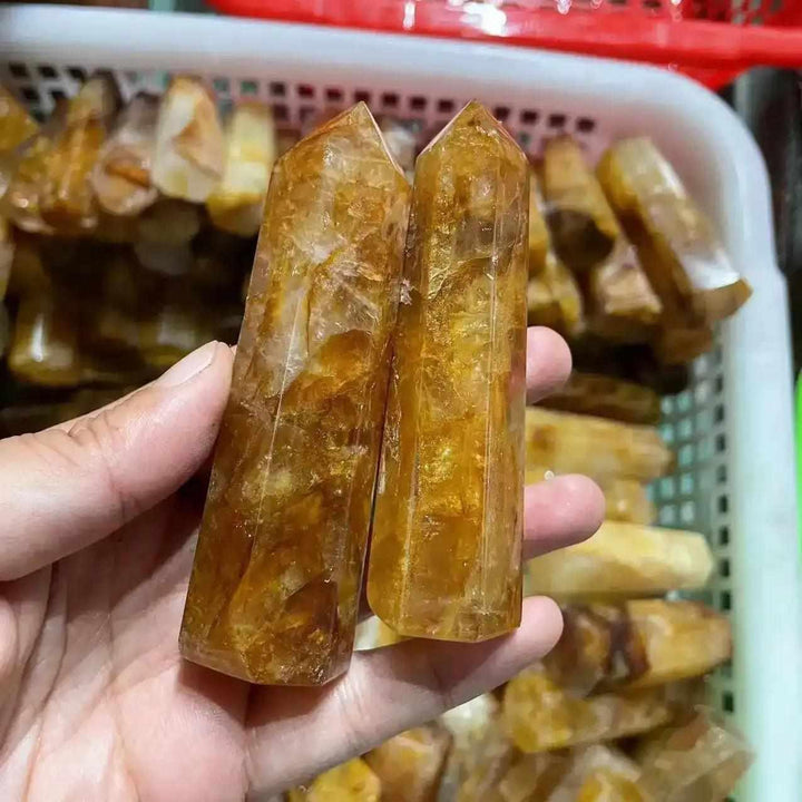 Two polished Golden Healer Quartz obelisks with warm yellow iron inclusions, held to show their hexagonal crystal points.