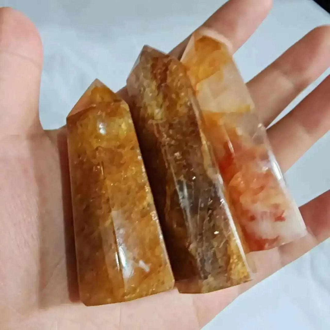 Three polished Golden Healer Quartz obelisks with warm yellow iron inclusions held in a hand for energy and clarity.