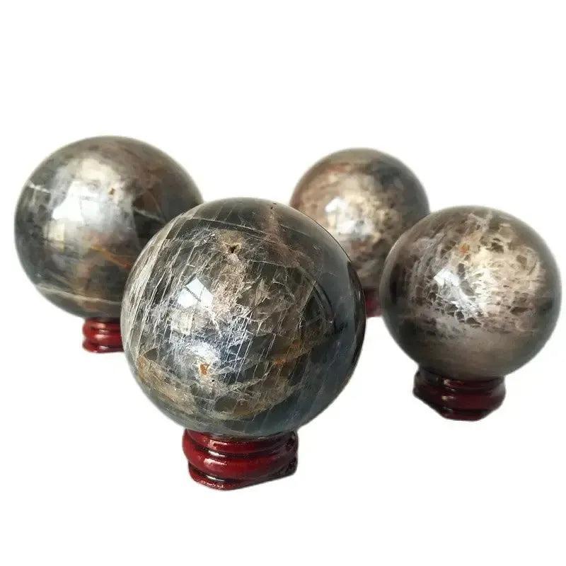 Four polished Gray Moonstone crystal spheres with silvery shimmer and adularescence on red wooden stands from Crystal Destiny.