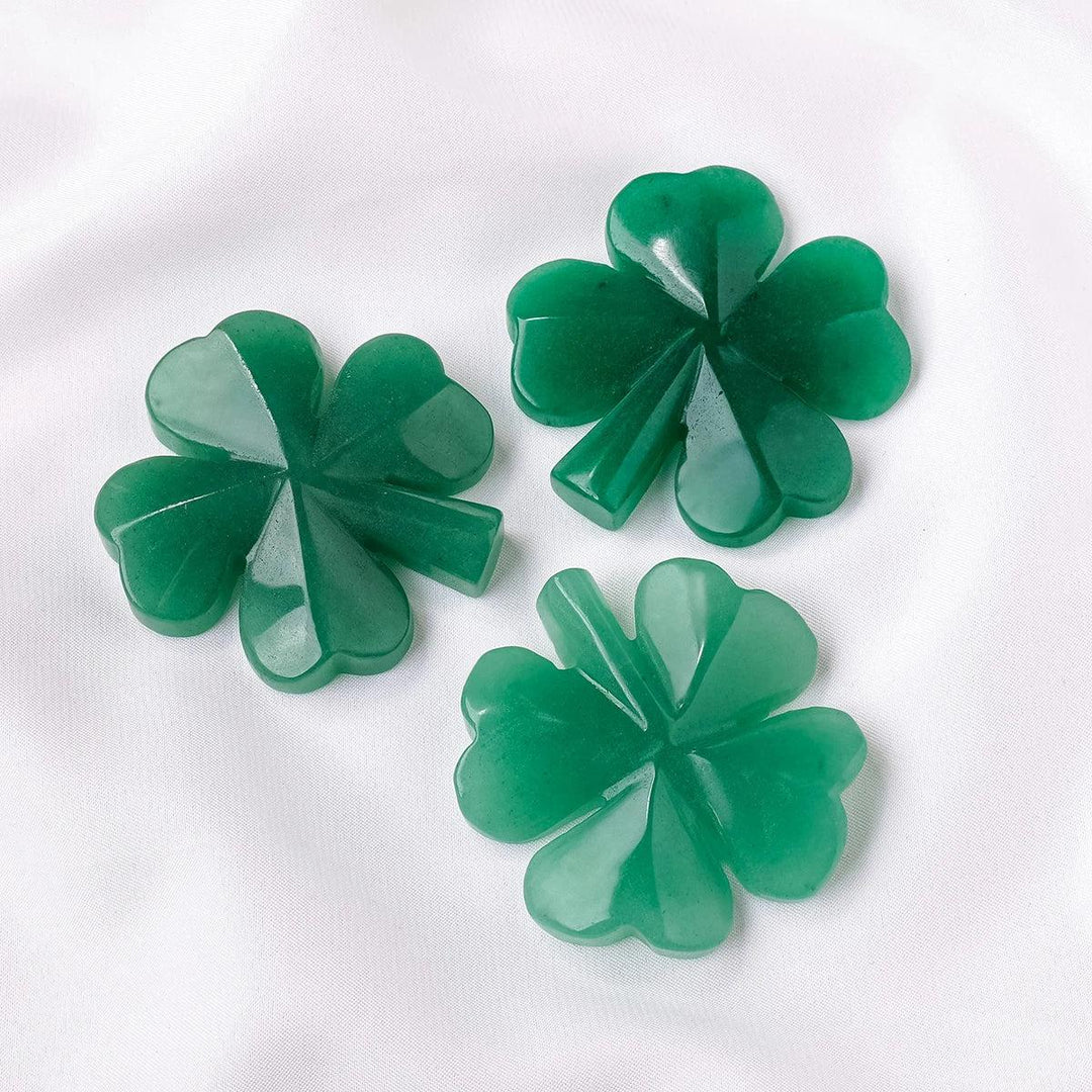 Three polished green aventurine four-leaf clover carvings, symbolizing luck and good fortune, on a white surface.