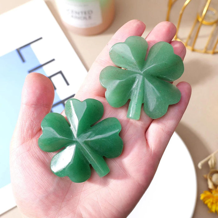 Two green aventurine four-leaf clover carvings, hand-polished and smooth, held in a palm.