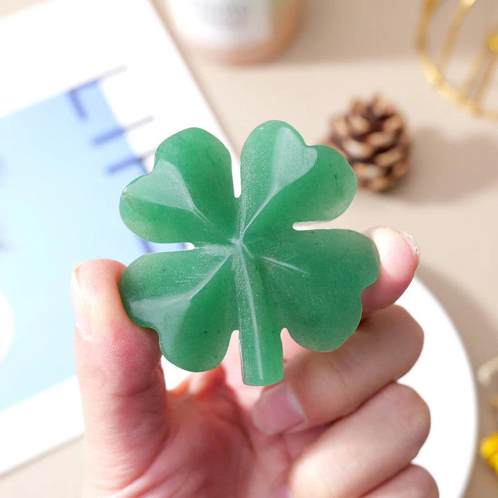 Hand holding a smooth, vibrant green aventurine four-leaf clover carving, symbolizing luck and abundance.