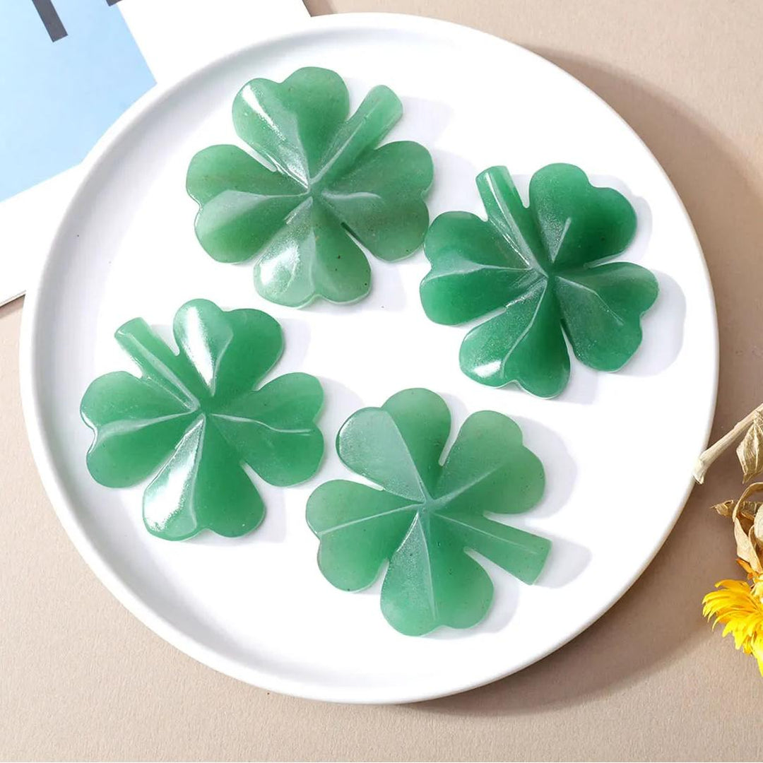 Four polished green aventurine four-leaf clover carvings on a white plate, symbolizing luck and abundance.