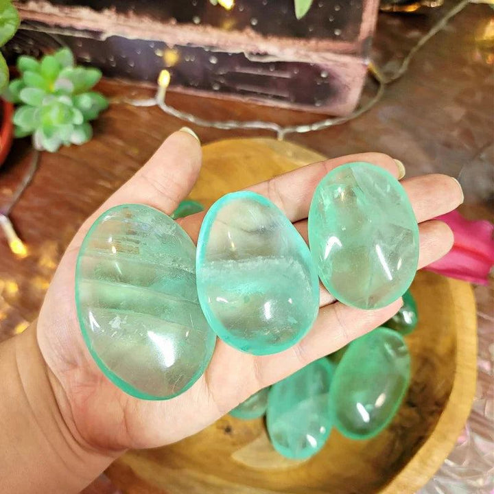 Polished clear green fluorite palm stones held in hand, showing natural healing crystal details.