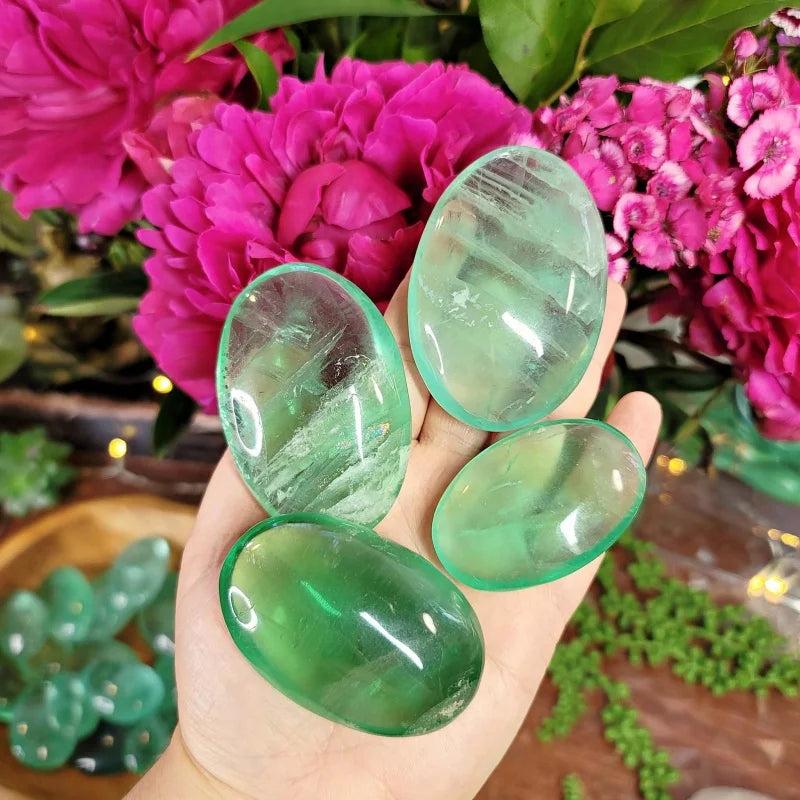 Polished green fluorite palm stones held in hand, showing natural translucent healing crystals.