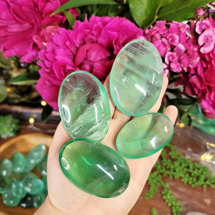 Polished green fluorite palm stones held in hand, showing natural translucent healing crystals.