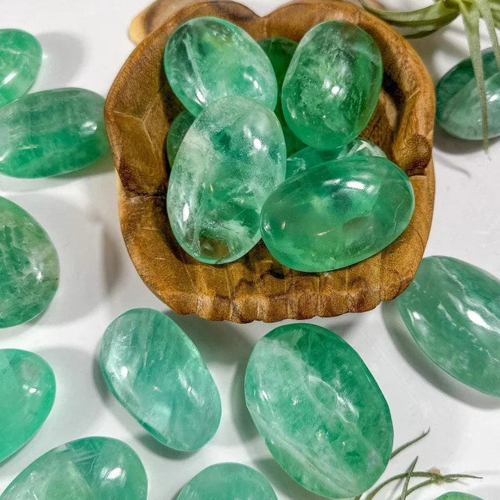 Polished green fluorite palm stones with healing energy in a wooden bowl.