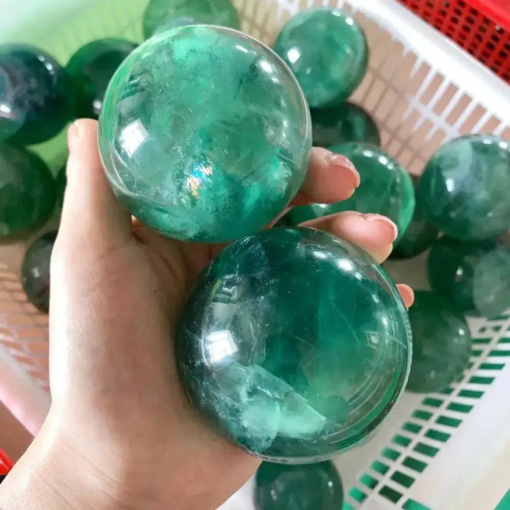 Hand holding two vibrant green fluorite spheres, promoting creativity and inspiration.