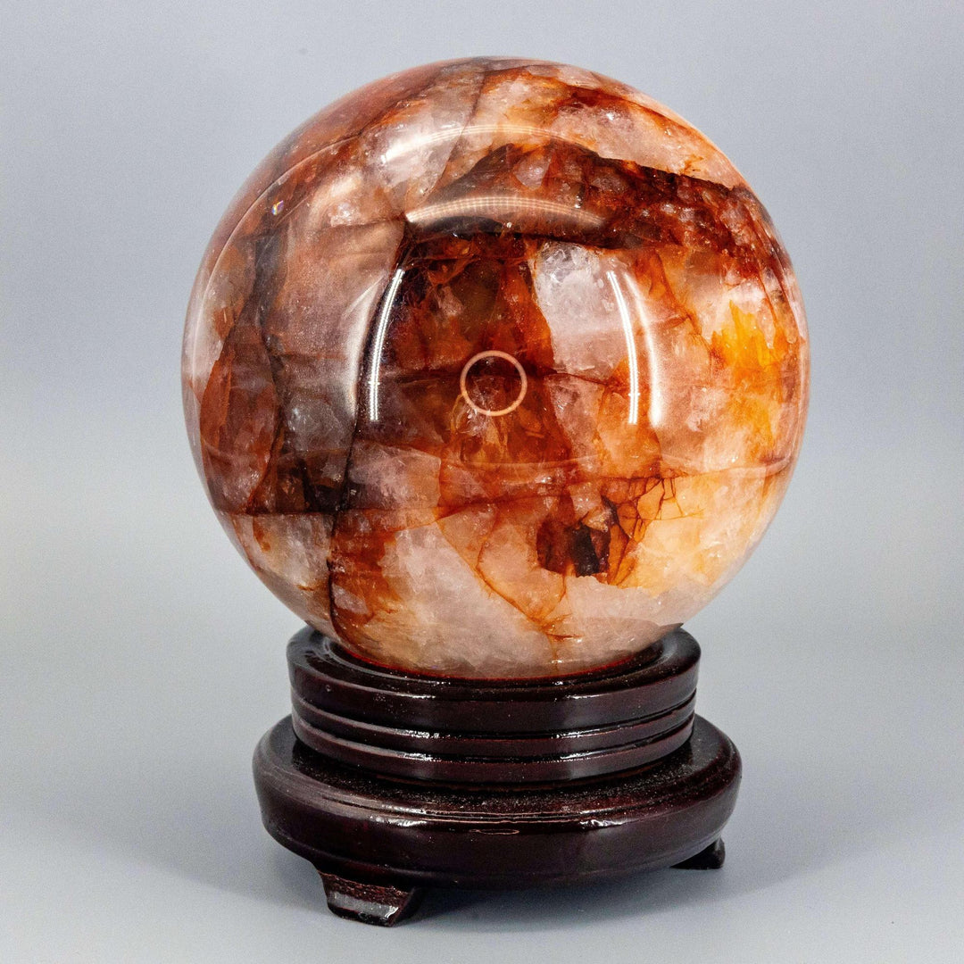Commanding 158mm Hematoid "Fire" Quartz Sphere radiating grounding and amplifying energy, on a dark wood stand.