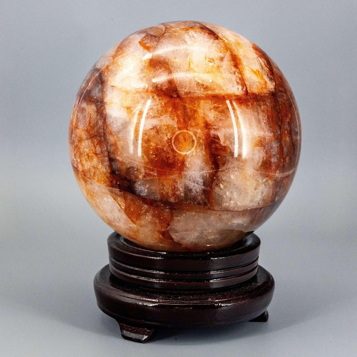 Commanding 158mm Hematoid "Fire" Quartz Sphere radiating grounding and amplifying energy on a dark wood stand.
