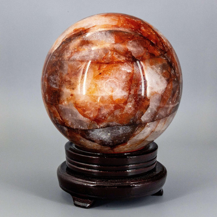 Commanding 158mm Hematoid "Fire" Quartz Sphere radiating grounding and amplifying energy, on a dark wooden stand.
