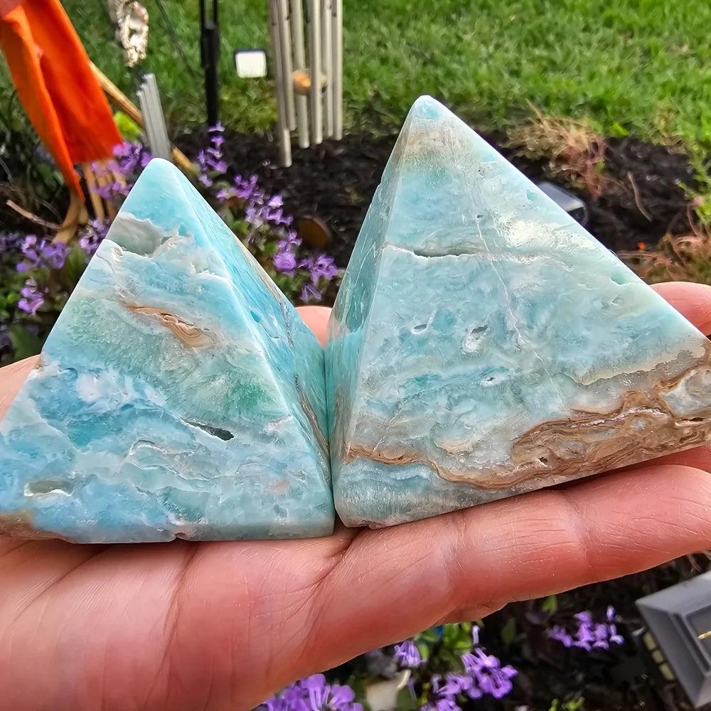 Two sky blue Hemimorphite Crystal Pyramids with natural white and brown banding held in a hand.
