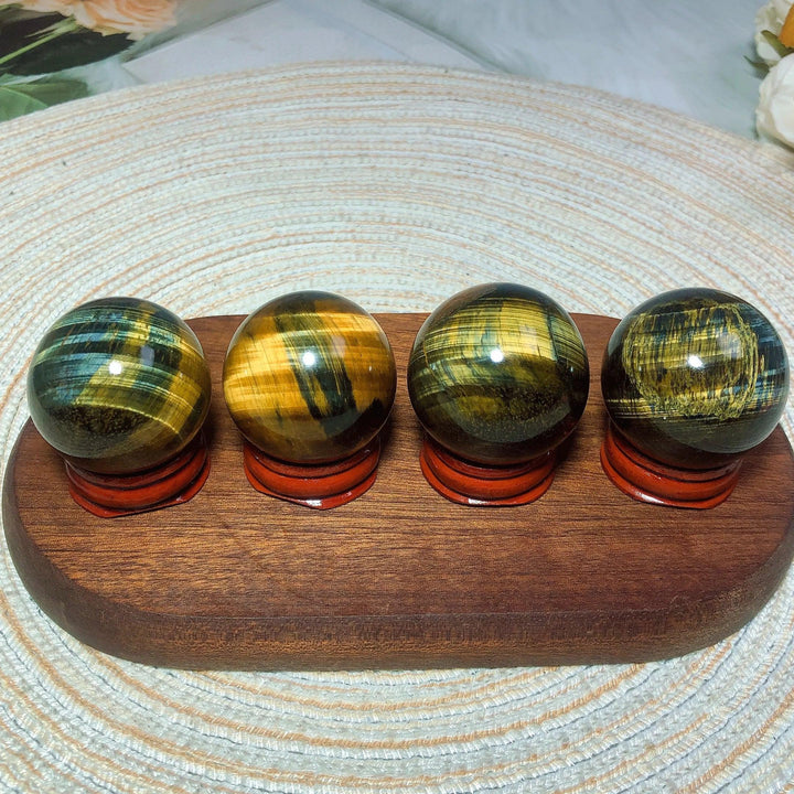 Four polished Blue and Yellow Tiger Eye crystal spheres on wooden stands, perfect for healing and home decor.