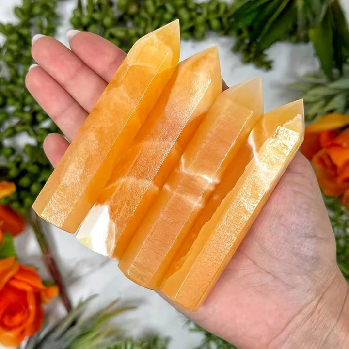 Four golden Honey Calcite Crystal Towers held in hand, showing natural banding for solar plexus healing.