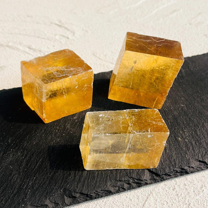 Three radiant Honey Calcite cubes, glowing with warm amber hues, on a dark slate surface.