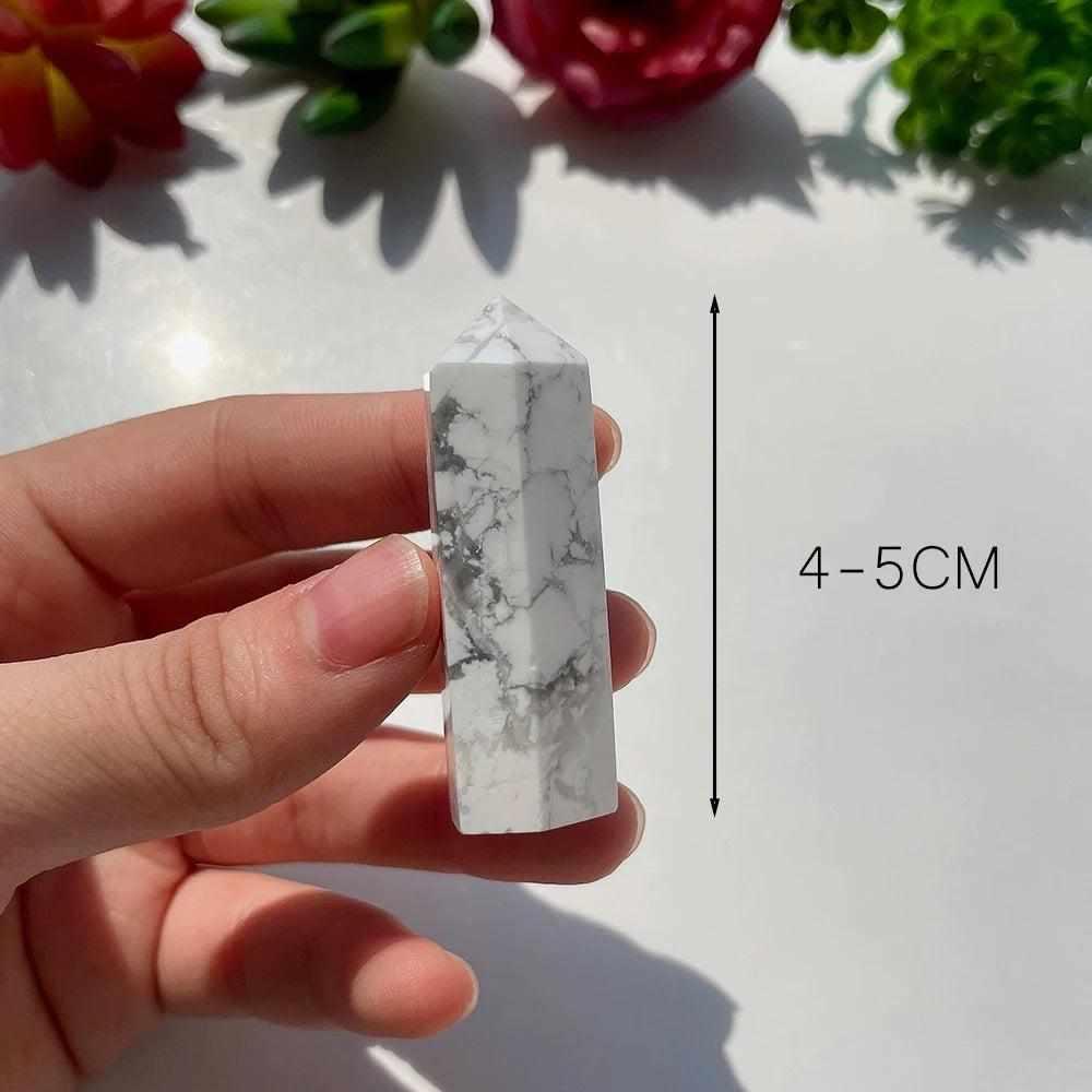 Polished white howlite tower point with gray veining, a calming crystal for the crown chakra, held in hand.