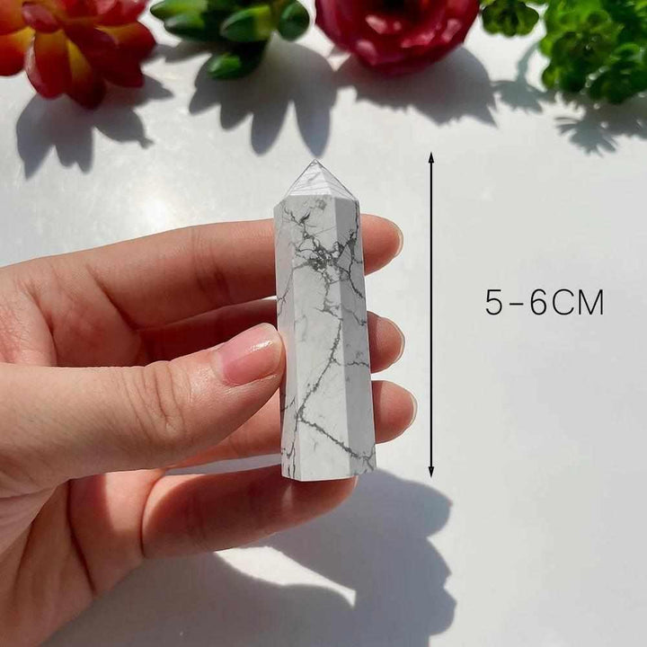 Polished white Howlite tower point with gray veining, held in hand to show its calming 5-6cm size for crown chakra healing.