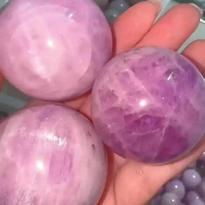 Polished pink and lilac Kunzite spheres held in hand, perfect for heart chakra healing and emotional calm.