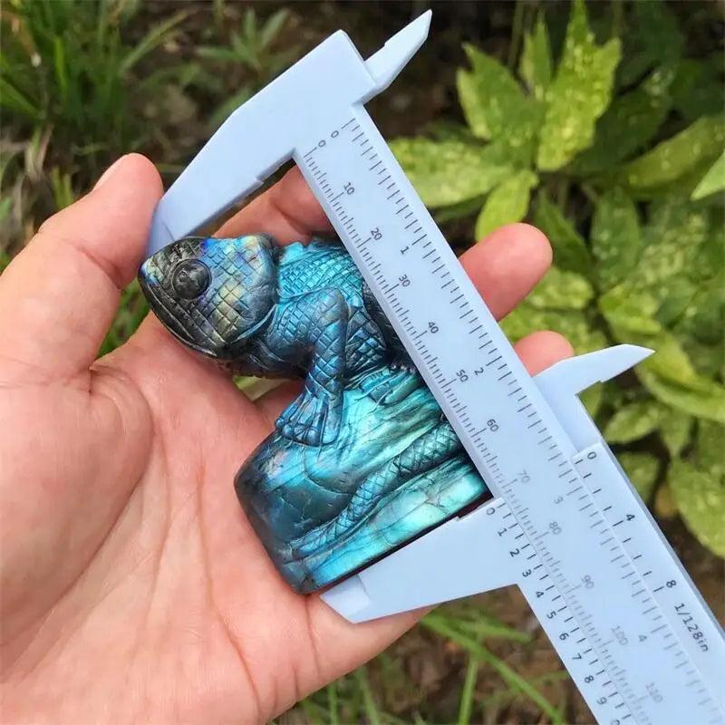 Iridescent blue-green Labradorite Crystal Carved Lizard Statue, 70mm, held with a caliper, showcasing its labradorescence.