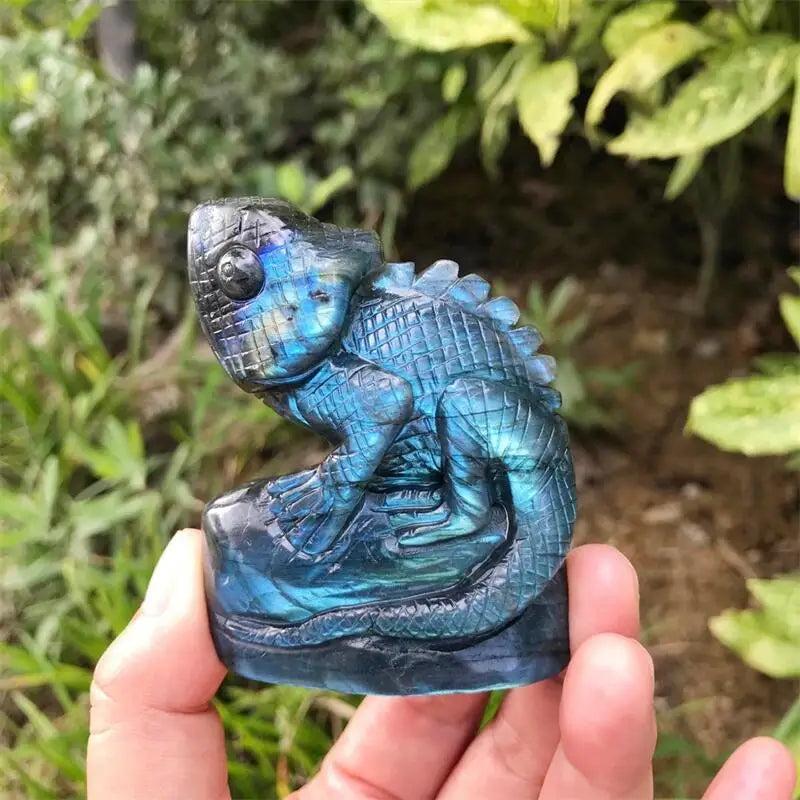 Iridescent blue and teal Labradorite crystal carved into a detailed lizard figurine, held in a hand outdoors.