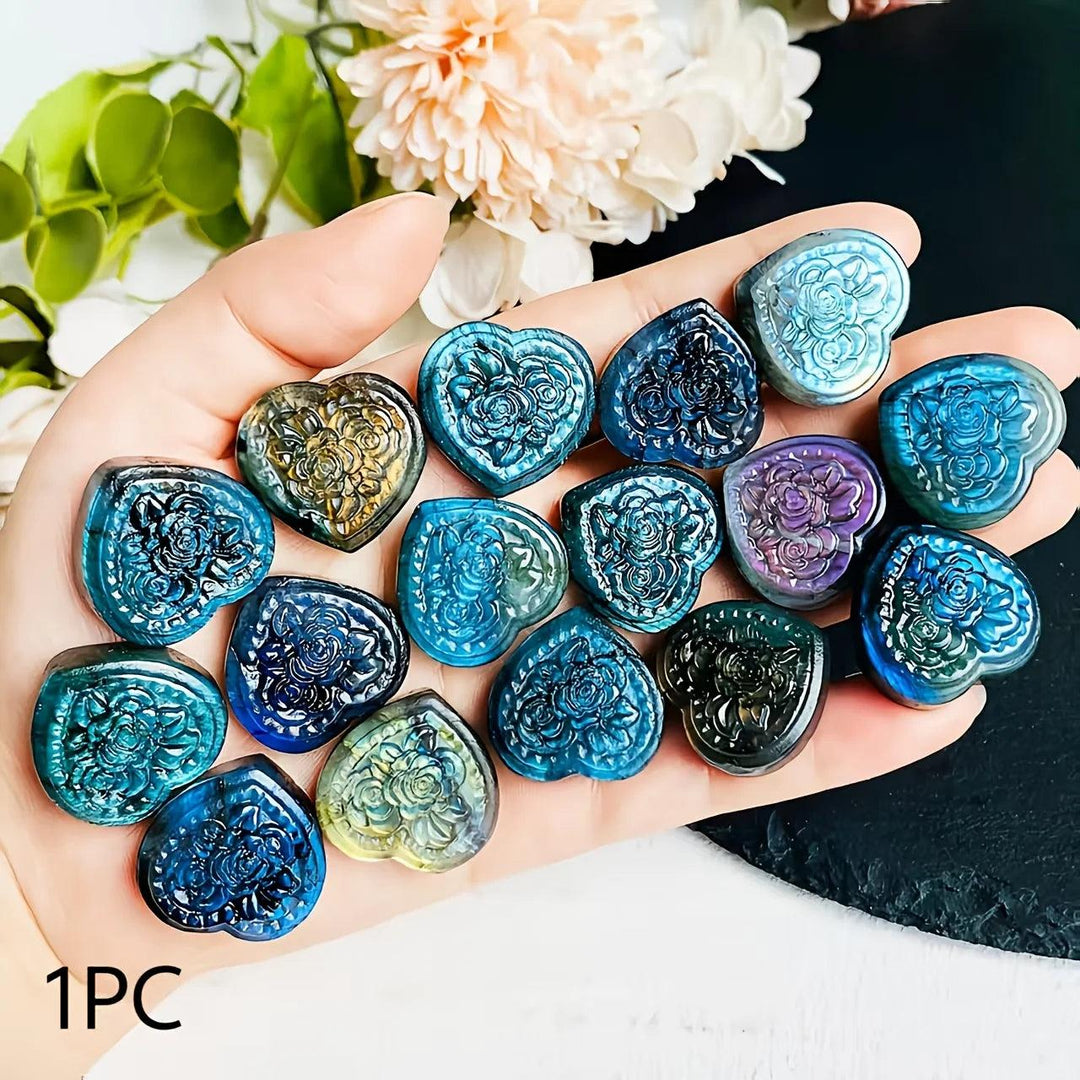 Hand holding polished Labradorite crystal heart pendants with intricate rose carvings and shimmering blue and gold flashes.