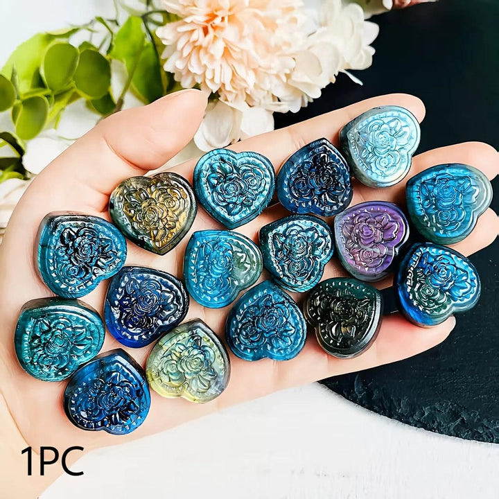 Hand holding polished Labradorite crystal heart pendants with intricate rose carvings and shimmering blue and gold flashes.