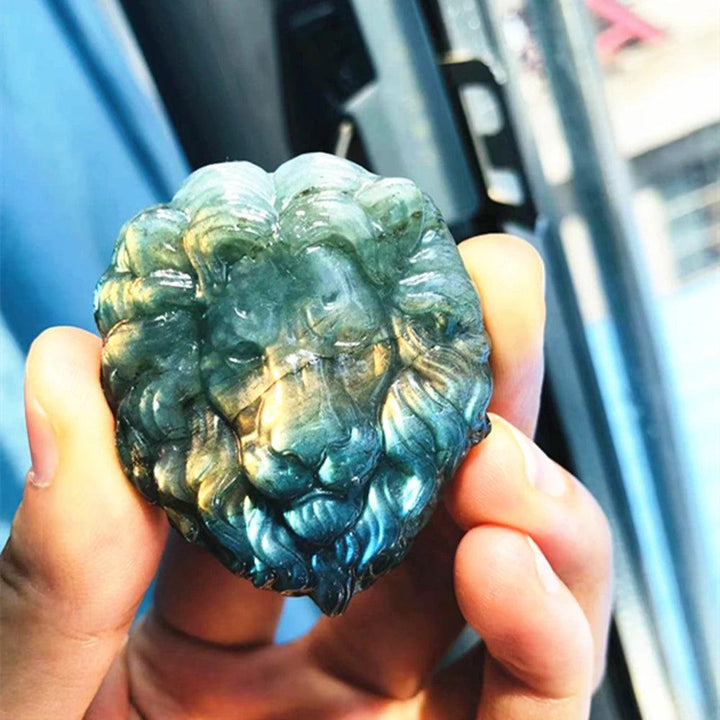 Polished labradorite lion head carving with iridescent blue, green, and gold flash, held in hand. Strength, courage, intuition.