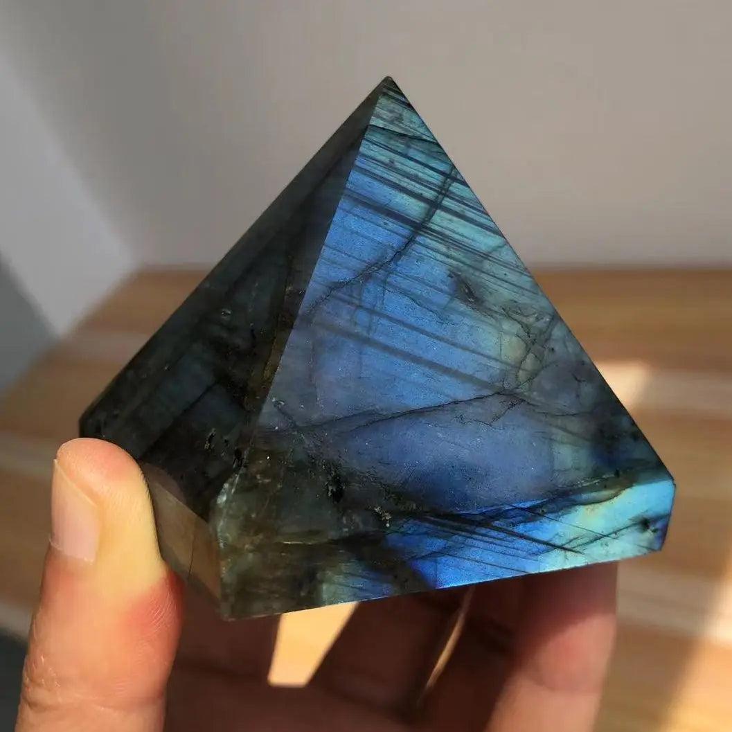 Polished Labradorite crystal pyramid with iridescent blue and teal flashes, held in a hand.