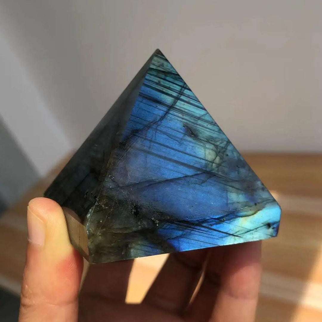 Polished Labradorite crystal pyramid with iridescent blue and teal flashes, held in a hand.