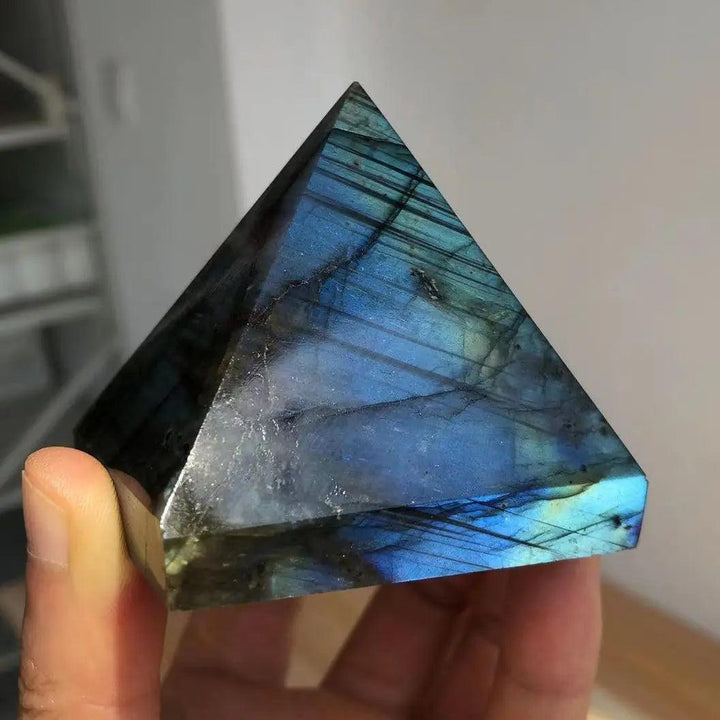 Polished Labradorite crystal pyramid with iridescent blue, teal, and gold flashes, held in a hand.