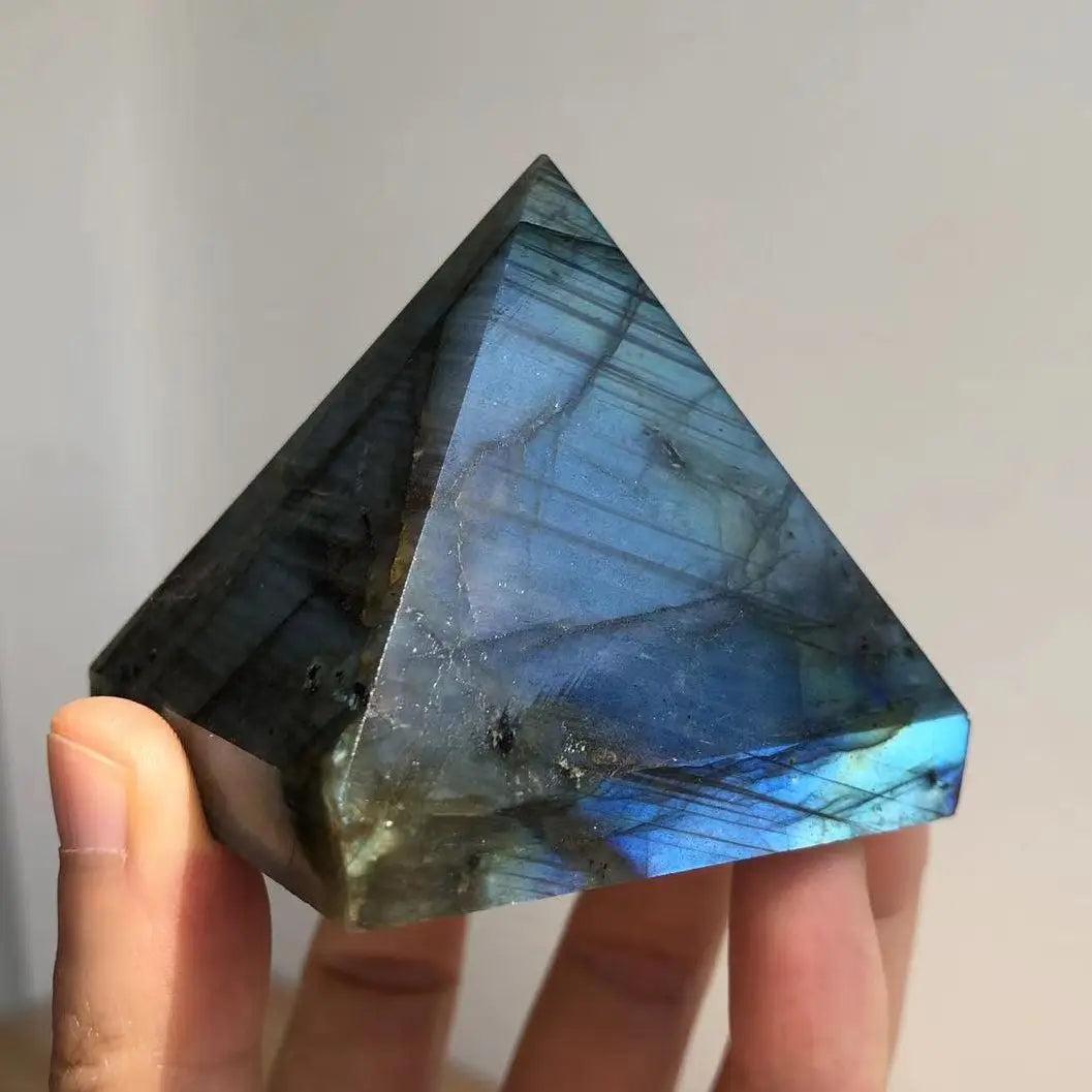 Hand holding a polished Labradorite crystal pyramid with iridescent blue and grey flashes.