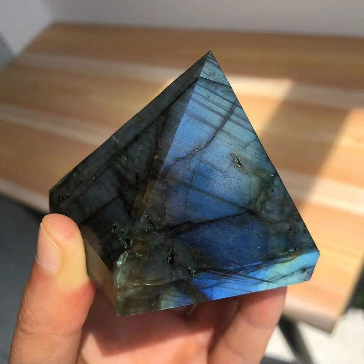 Polished Labradorite crystal pyramid with iridescent blue and teal flashes, held in a hand.