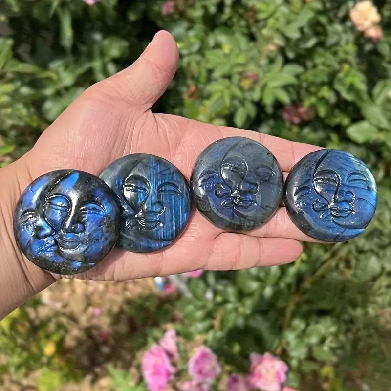 Four shimmering labradorite crystal moon and sun carvings, displaying iridescent blues and golds, held in a hand.