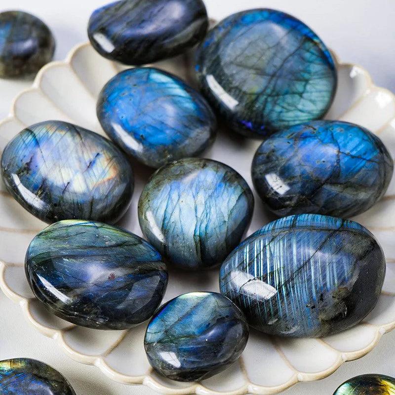 Polished blue labradorite palm stones with iridescent flash on a decorative plate.