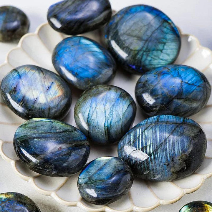 Polished blue labradorite palm stones with iridescent flash on a decorative plate.