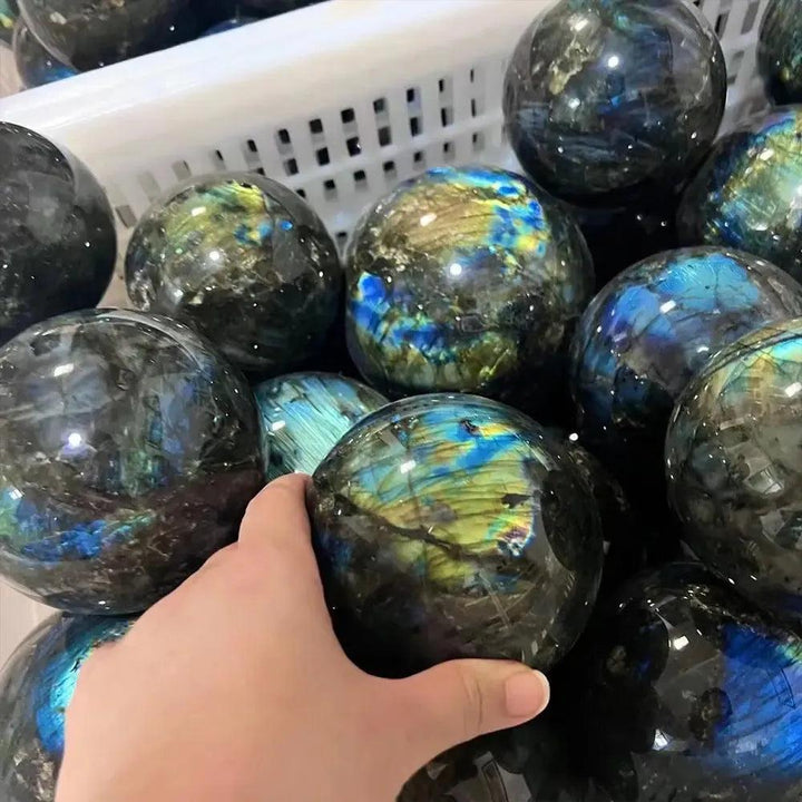 Hand holding a polished Labradorite crystal sphere with vibrant blue, green, and gold flashes from Crystal Destiny.