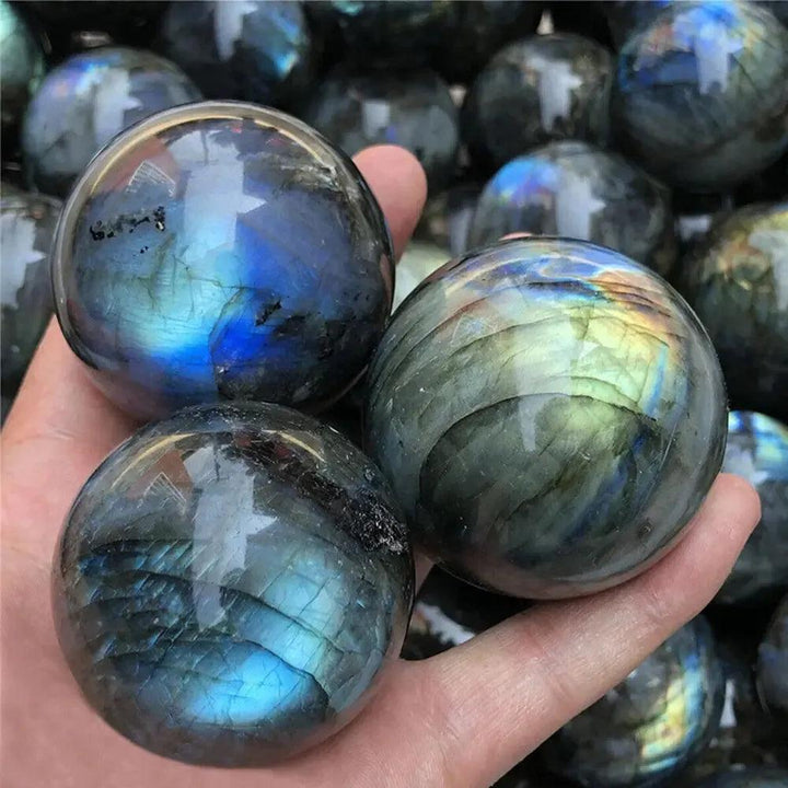 Hand holding three polished Labradorite crystal spheres with blue, green, and gold iridescence from Crystal Destiny.