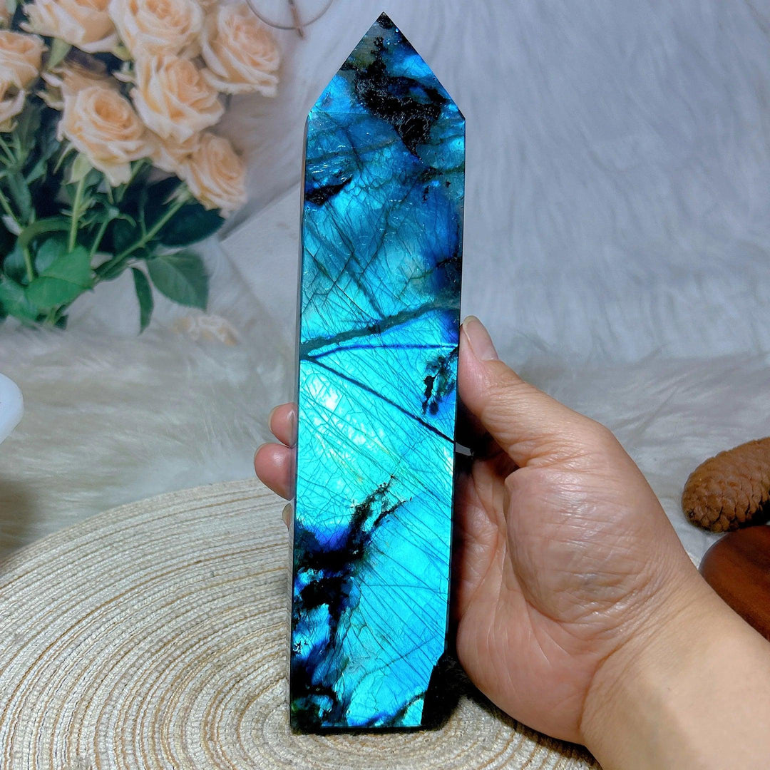 Hand holding a tall, polished Labradorite crystal tower with vibrant blue, teal, and black flashes.