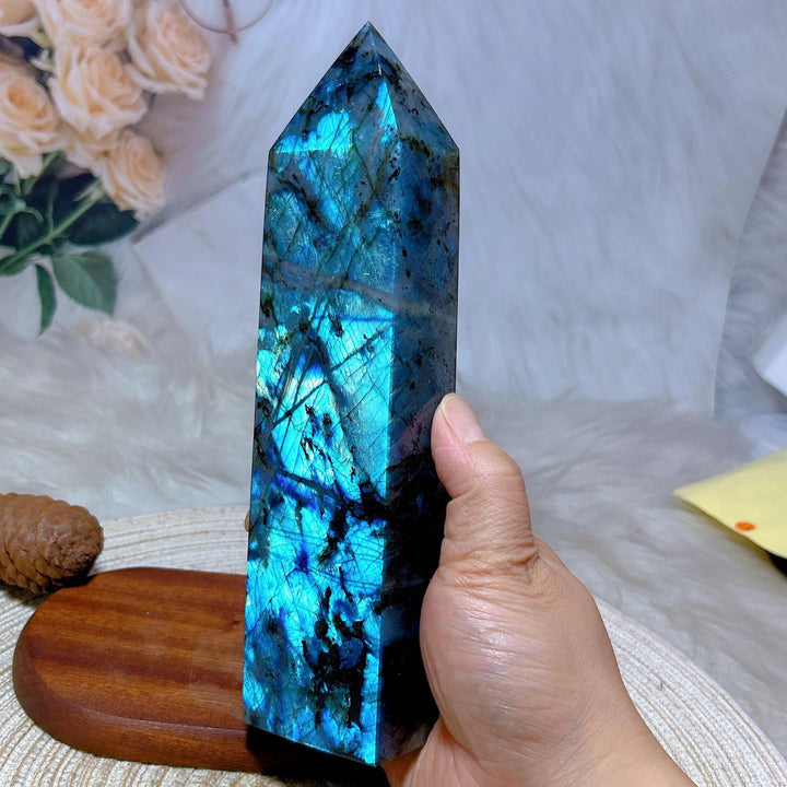 Hand holding a tall, polished Labradorite crystal tower with vibrant blue and teal labradorescence.
