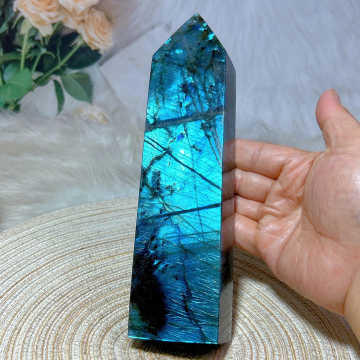 Polished Labradorite crystal tower with vibrant blue, teal, and gold labradorescence, held by a hand.