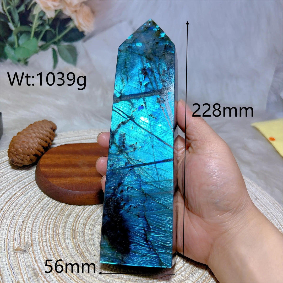 Large polished Labradorite crystal tower with vibrant blue-green flash, held in hand, showing size and weight.