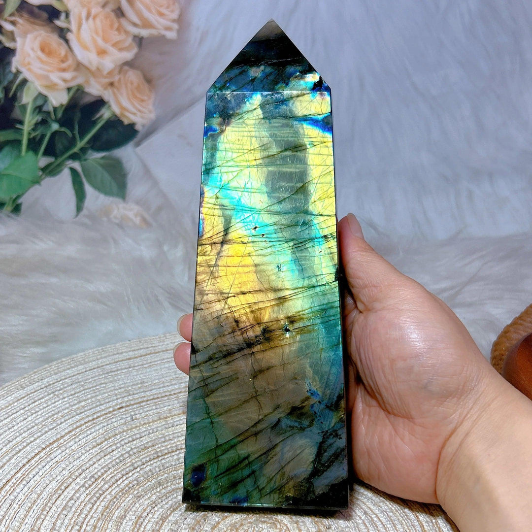 Labradorite crystal tower with vivid blue, teal, and gold labradorescence, held in a hand.