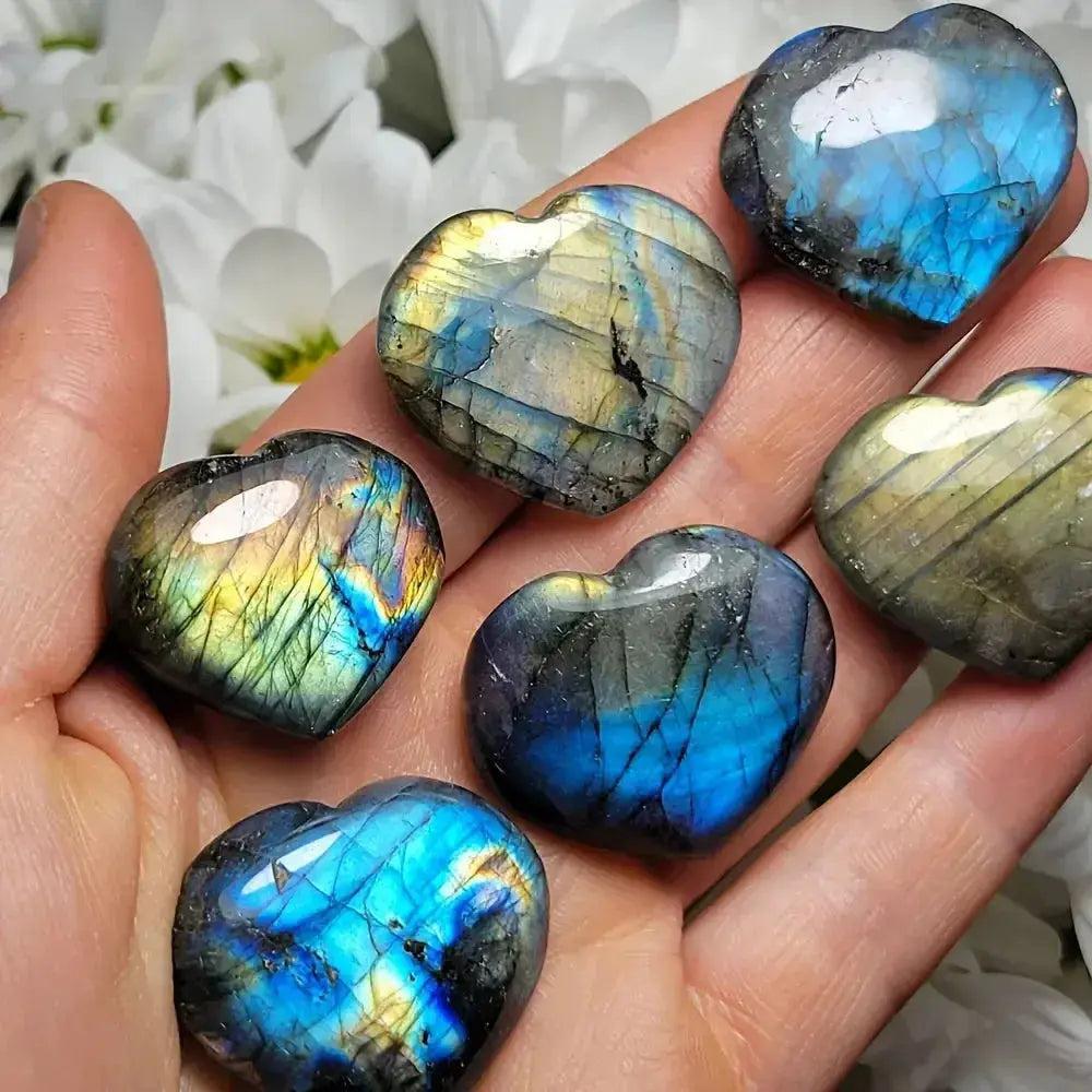 Hand holding six iridescent blue and gold Labradorite heart carvings from Crystal Destiny.