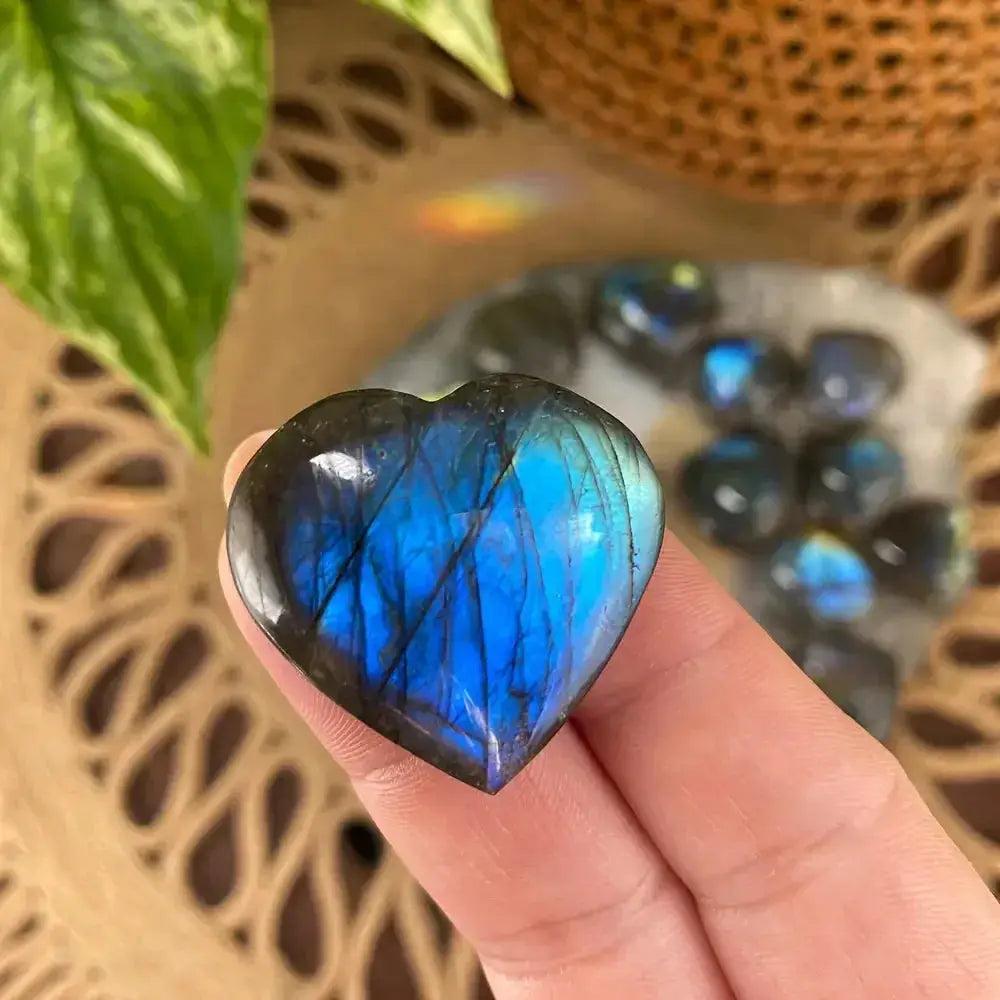 Labradorite heart carving from Crystal Destiny, showcasing vibrant blue and gold flashes, held in a hand.