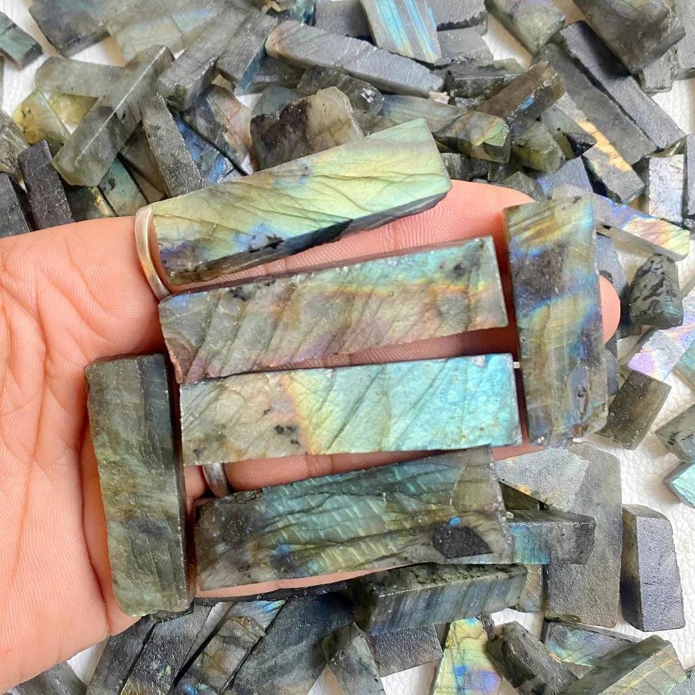 Hand holding raw Labradorite crystal sticks with vibrant blue, gold, and green spectral flashes for transformation.