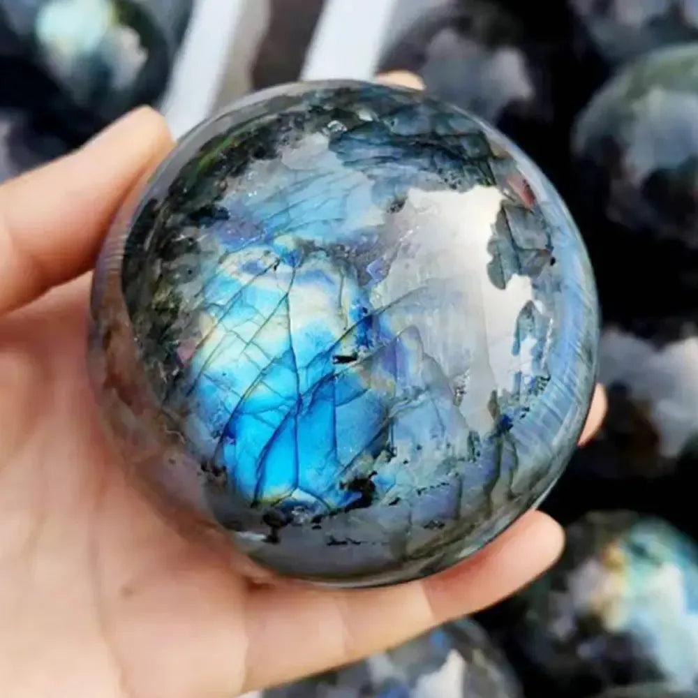 Polished Labradorite sphere, held in hand, showcasing vibrant blue, green, and gold iridescent flash from Crystal Destiny.